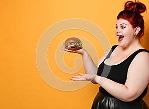 Happy overweight fat woman happy hold big burger cheeseburger sandwich with beef in hand laughing on yellow