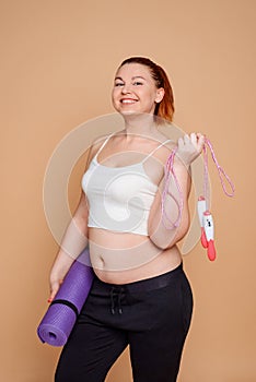 Happy overweight woman holding a mat and a jump rope