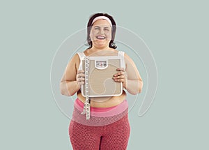 Happy overweight woman in sportswear holding bathroom scale