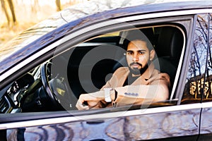 Happy owner. Handsome bearded man sitting relaxed in his newly bought car looking out the window smiling joyfully