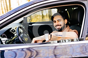 Happy owner. Handsome bearded man sitting relaxed in his newly bought car looking out the window smiling joyfully