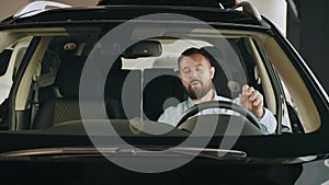 Happy owner. Handsome bearded mature man sitting relaxed in his newly bought car looking out the window smiling joyfully