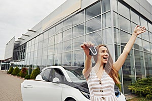 Happy owner of new car. Female driver holds keys from automobile in hand