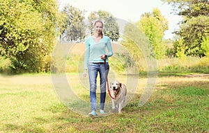 Happy owner woman and Golden Retriever dog walking together in park