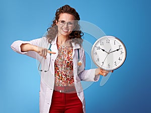 Happy paediatrician doctor pointing at clock on blue
