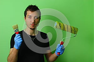 Happy painter decorator holding a brush and roller in his hands on a background of painted green wall