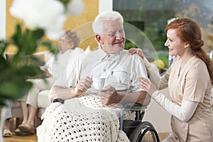Happy paralyzed senior man in a wheelchair drinking tea and a ca