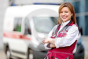 Happy paramedic with phonendoscope at emergency car background