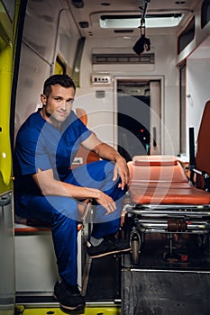 Happy paramedic sits in the ambulance car on the background
