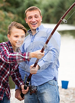 Happy parent and boy fishing together on freshwater lake