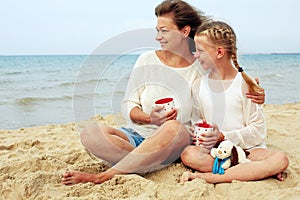 Happy parent and child drinking tea on the beach