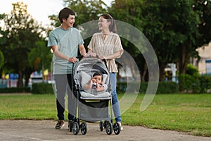 happy parent (father and mother) talking and pushing infant baby stroller and walking in park