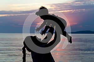 Happy parent mother with baby silhouette at the beach at sunset. Happy family summertime concept