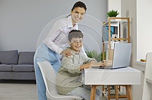 Happy parent or school teacher helping student boy while he uses laptop computer