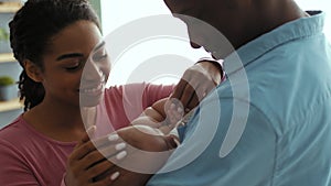 Happy parenthood. African american mother and father giving water to newborn baby from kid bottle