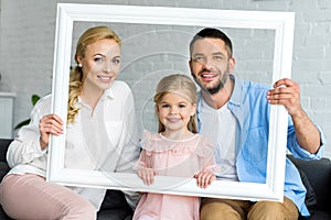 happy parents with adorable little daughter holding white frame and smiling