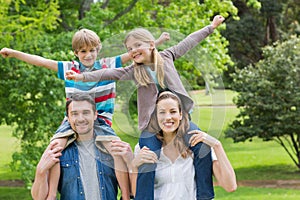 Happy parents carrying kids on shoulders at park