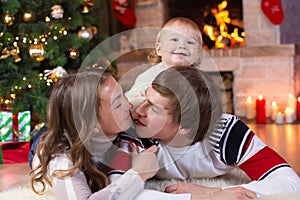 Happy parents and child boy have a fun near Christmas tree at home. Father, mother, son celebrating New Year together