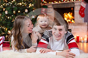 Happy parents and child boy have a fun near Christmas tree at home. Father, mother, son celebrating New Year together