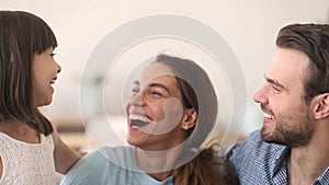 Happy parents and child daughter embracing laughing looking at camera