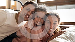 Happy parents and child daughter looking at camera on bed