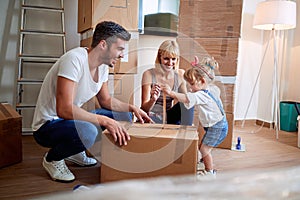 Happy parents with child moving in new home unpacking boxes