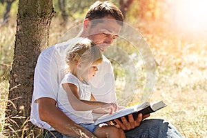 Happy parents with a child read the Bible in the nature park