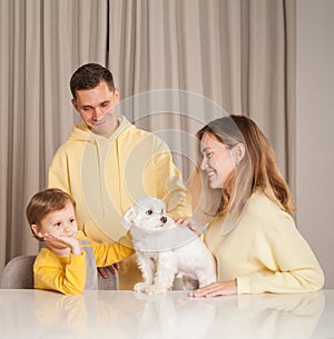 Happy parents with child son and white white small puppy pet at home