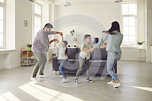 Happy parents and children dancing and having fun in the living-room of new apartment