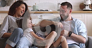 Happy parents with children laughing tickling relax on sofa together