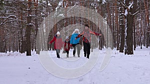 Happy parents and children run along snowy winter road in coniferous park and laugh on winter frosty day. Family games