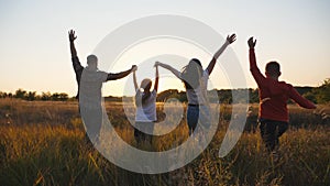 Happy parents with children run through summer grass field holding hands of each other and raising arms. Mommy and daddy