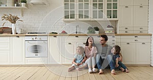 Happy parents and children talking laughing sit on kitchen floor