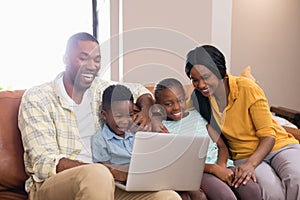 Happy parents and children using laptop while sitting on sofa