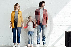 happy parents with cute little daughter holding hands while standing together