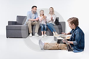 Happy parents and cute little sister applauding to boy playing guitar