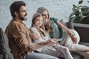 happy parents and daughter watching tv on sofa