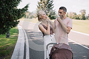 happy parents eating ice cream near baby carriage