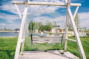 Happy parents enjoys swinging with two children on side the lake. Back view