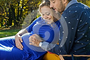 Happy parents expecting baby, touching belly, sitting on green grass