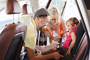 Happy parents fastening child with car seat belt