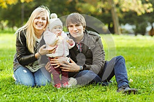 Happy parents with girl on green lawn in autumn park