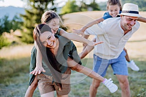 Happy parents giving their children piggyback ride in summer in nature.