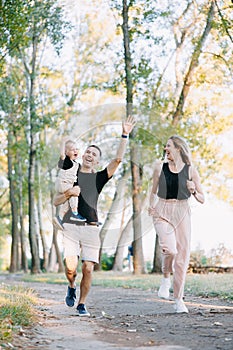 Happy parents have fun, laughing and running with his toddler boy in park