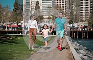 Happy parents holding hands with son and walking in sunny summer citi street, tender family moment. photo