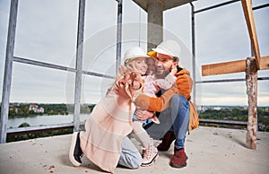 Happy parents hugging daughter in building under construction.