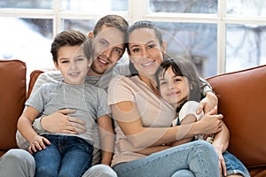 Happy parents with kids bonding looking at camera on sofa