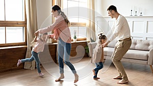 Happy parents and kids daughters dancing spinning together at home