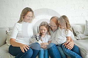 Happy parents and kids having fun with little dog pet sitting together on sofa