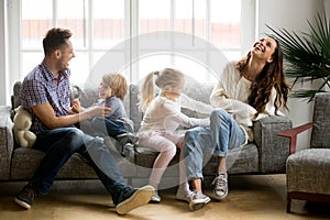 Happy parents and kids having fun tickling sitting on sofa